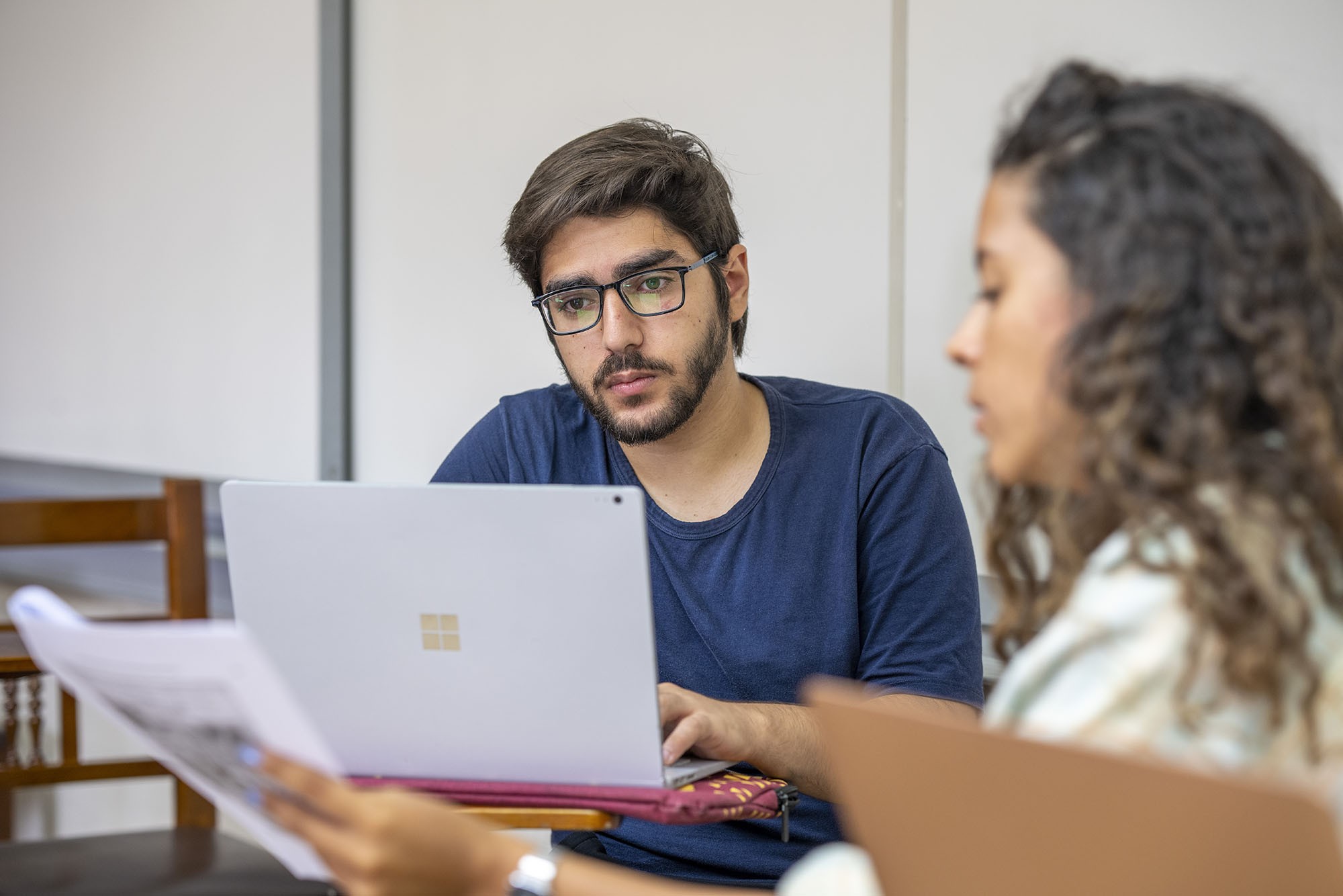 a boy and girl sitting in a classroom looking at a laptop